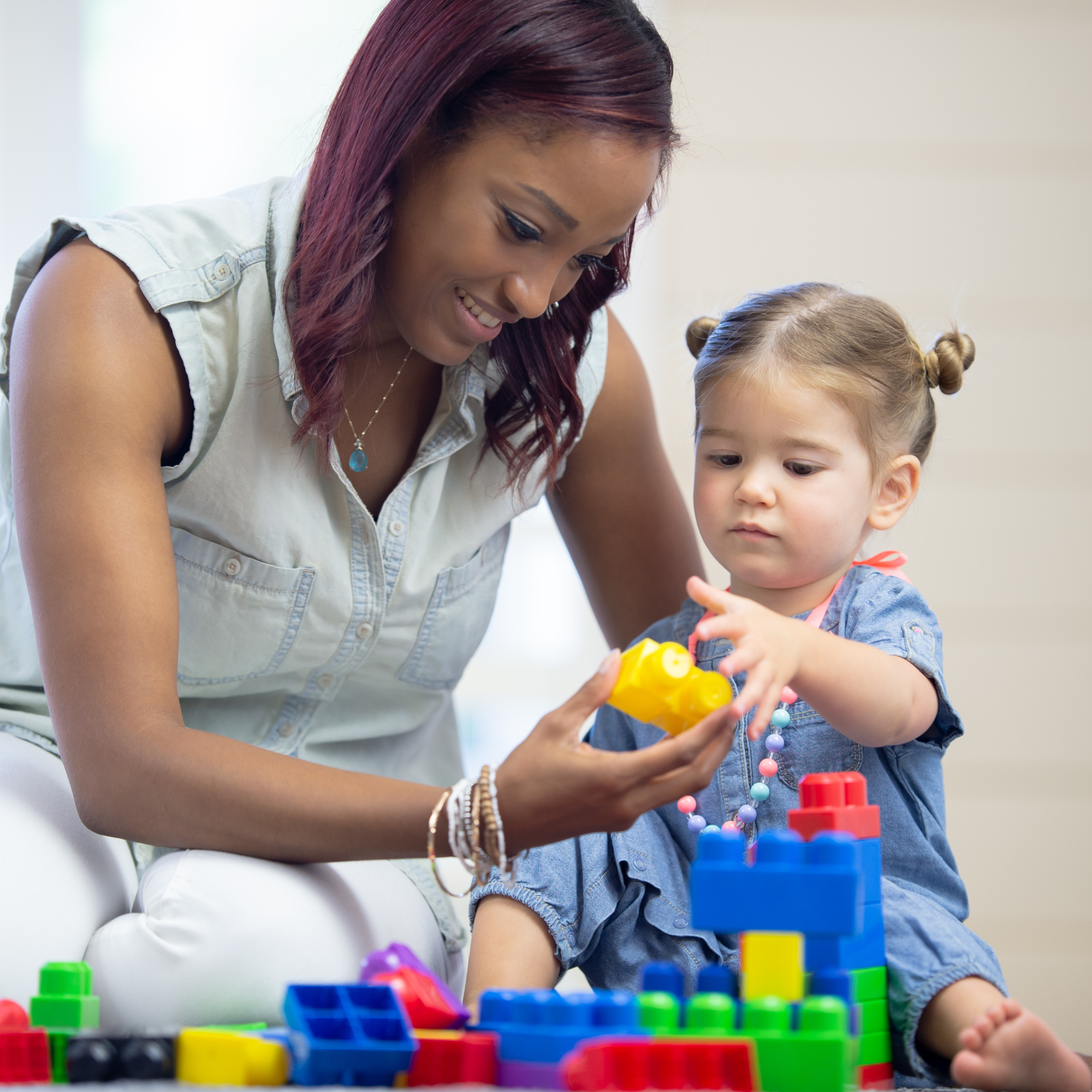 A woman and child play joyfully with colorful toy blocks. The woman, smiling, guides the focused child. The scene conveys warmth and learning.