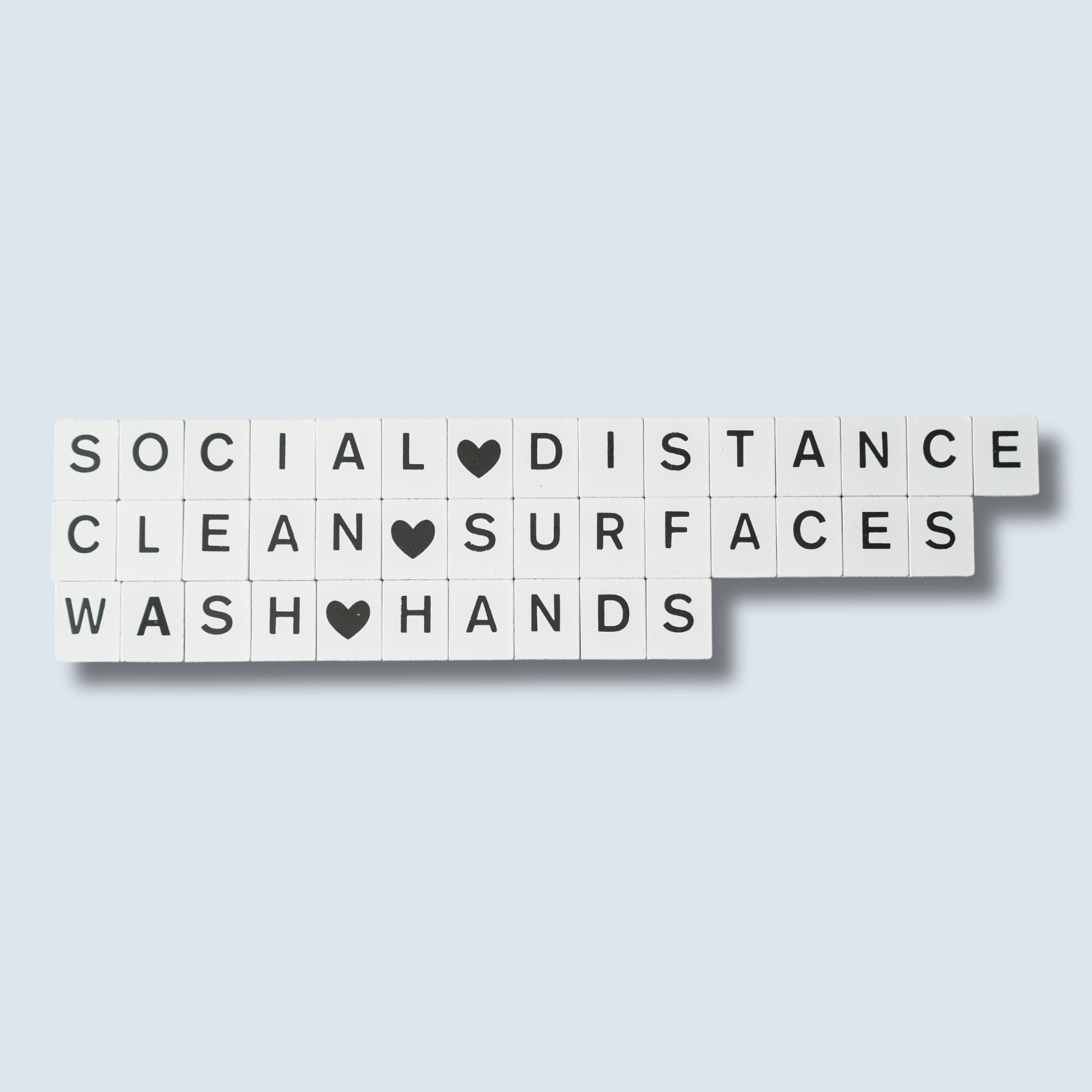 White tiles with black letters display health guidelines: "Social Distance," "Clean Surfaces," and "Wash Hands," with hearts as spaces. Calm tone.