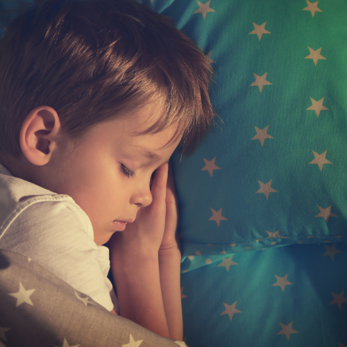 Young boy peacefully sleeping, head resting on a star-patterned pillow. Warm lighting creates a serene, cozy atmosphere.